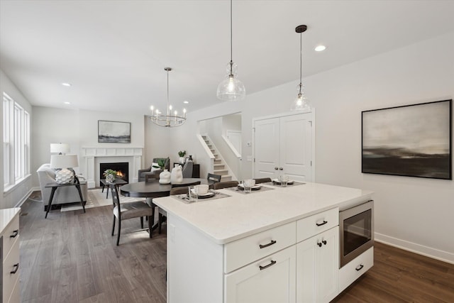 kitchen with dark wood-style floors, stainless steel microwave, white cabinets, a lit fireplace, and baseboards