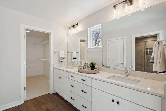 bathroom with a stall shower, double vanity, a sink, and wood finished floors