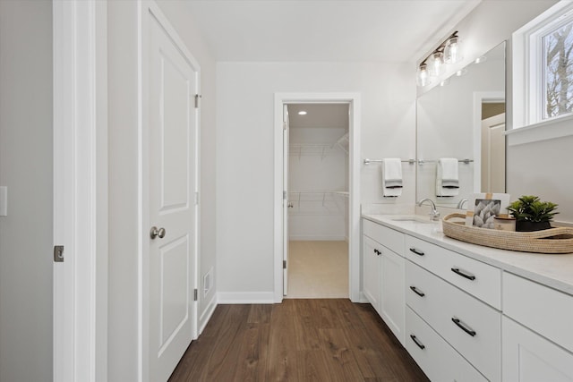 full bath featuring a spacious closet, vanity, baseboards, and wood finished floors