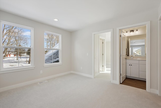 unfurnished bedroom featuring ensuite bath, carpet, visible vents, and baseboards