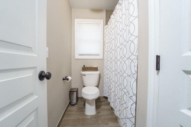 bathroom featuring toilet, a shower with shower curtain, wood finished floors, and baseboards