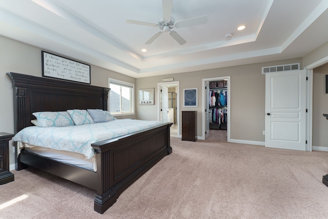 bedroom featuring a walk in closet, light carpet, a tray ceiling, visible vents, and recessed lighting