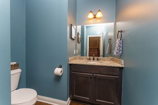 bathroom with baseboards, wood finished floors, toilet, and vanity