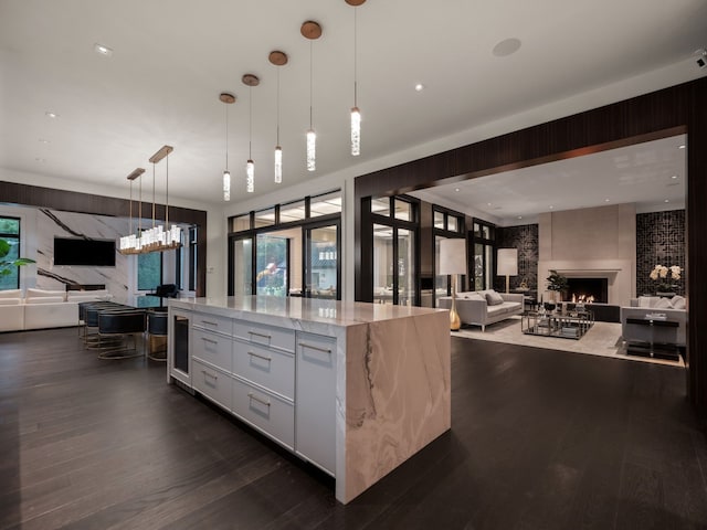 kitchen with white cabinetry, light stone counters, dark hardwood / wood-style floors, pendant lighting, and a fireplace