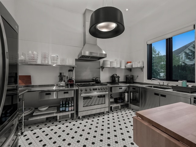 kitchen featuring high end range, wall chimney range hood, sink, fridge, and stainless steel counters