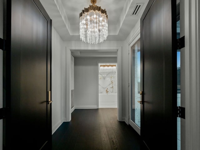 hallway featuring a chandelier, a raised ceiling, and dark wood-type flooring