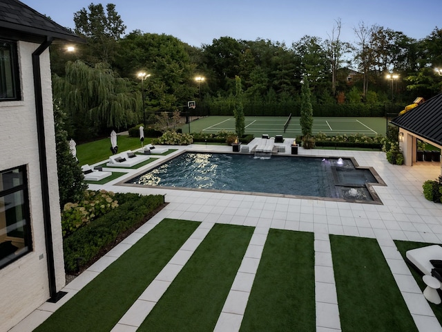 pool at dusk featuring pool water feature, tennis court, and a patio