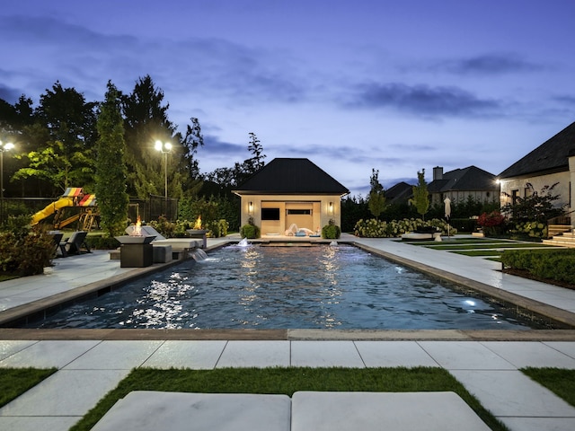 pool at dusk featuring pool water feature, an outbuilding, and a patio