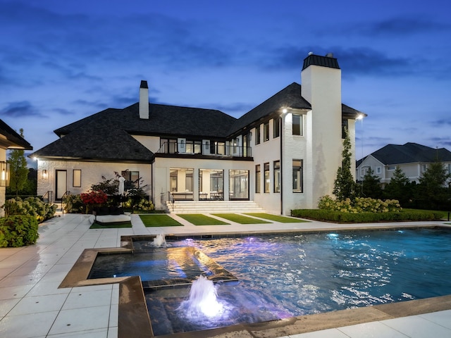 back house at dusk with pool water feature and a balcony