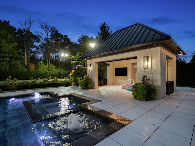 pool at dusk with pool water feature, an in ground hot tub, and a patio