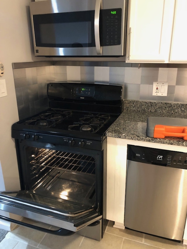 kitchen with light tile patterned floors, dark stone countertops, decorative backsplash, white cabinets, and appliances with stainless steel finishes