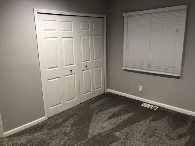 unfurnished bedroom featuring dark carpet and a closet