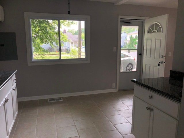 kitchen featuring light tile patterned flooring, dark stone countertops, white cabinetry, and electric panel