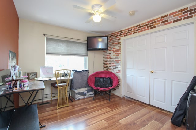 home office featuring ceiling fan, light wood-type flooring, and brick wall