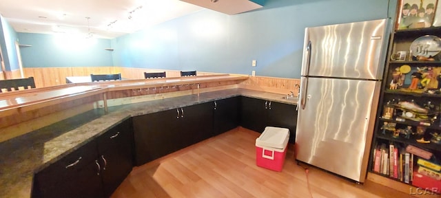 kitchen featuring wooden walls, light hardwood / wood-style floors, light stone countertops, and stainless steel refrigerator