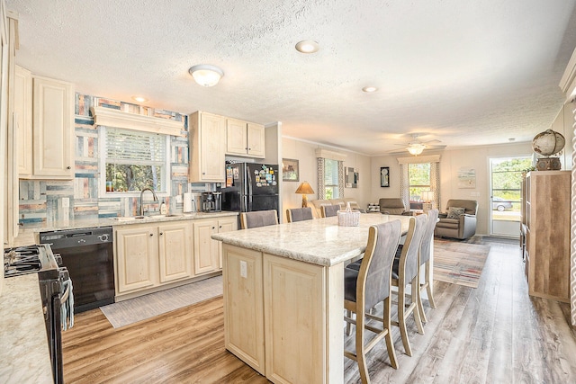 kitchen featuring a kitchen breakfast bar, tasteful backsplash, sink, black appliances, and light hardwood / wood-style floors