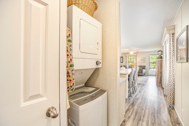 laundry area featuring crown molding, stacked washer / dryer, and light hardwood / wood-style flooring