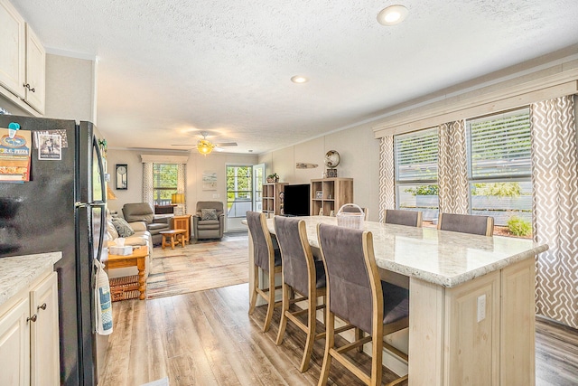 dining space with ceiling fan, light wood-type flooring, a textured ceiling, and ornamental molding