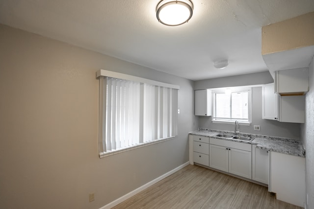 kitchen featuring white cabinets, light hardwood / wood-style flooring, light stone countertops, and sink