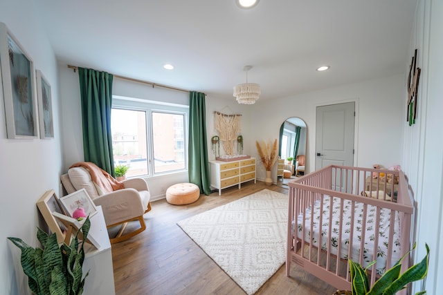 bedroom with a chandelier, hardwood / wood-style flooring, and a nursery area