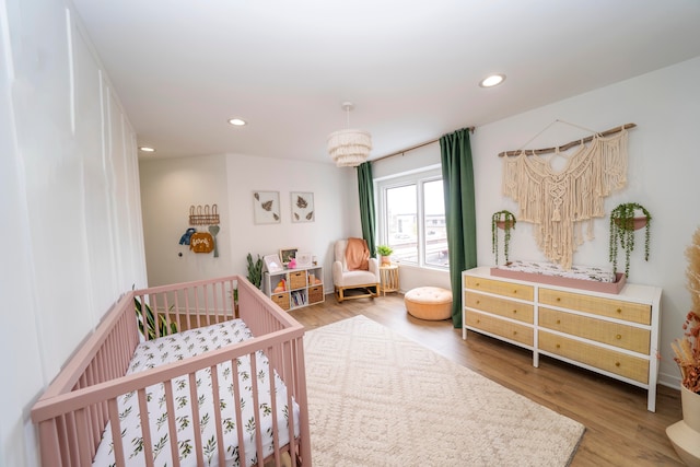 bedroom featuring hardwood / wood-style flooring, a crib, and a chandelier