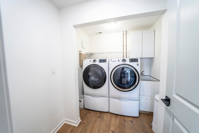 laundry area with cabinets, light wood-type flooring, sink, and washing machine and clothes dryer