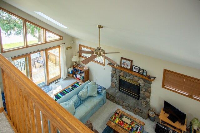 living area with ceiling fan, lofted ceiling with skylight, a fireplace, and carpet flooring