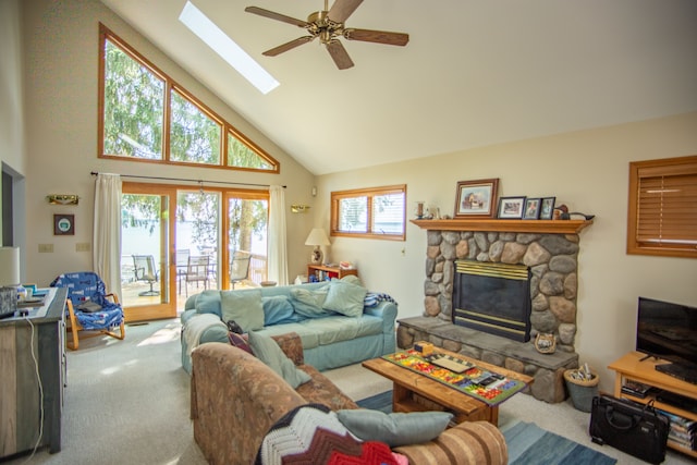 carpeted living room featuring high vaulted ceiling, a stone fireplace, a skylight, and a ceiling fan