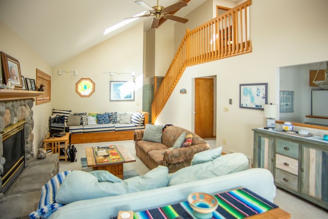 carpeted living area with ceiling fan, high vaulted ceiling, a fireplace, a skylight, and stairway