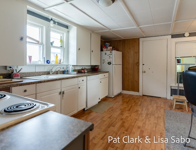 kitchen featuring white cabinetry, sink, wood walls, light hardwood / wood-style floors, and white appliances