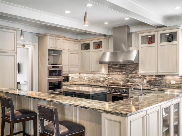 kitchen featuring stainless steel range, hanging light fixtures, wall chimney range hood, a kitchen breakfast bar, and dark stone countertops