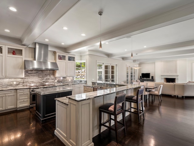 kitchen featuring wall chimney exhaust hood, light stone counters, dark hardwood / wood-style floors, pendant lighting, and a kitchen island