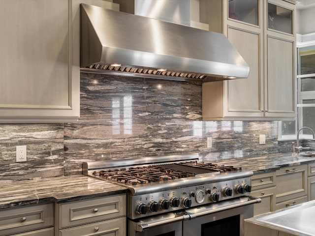 kitchen featuring decorative backsplash, dark stone counters, range with two ovens, and wall chimney exhaust hood