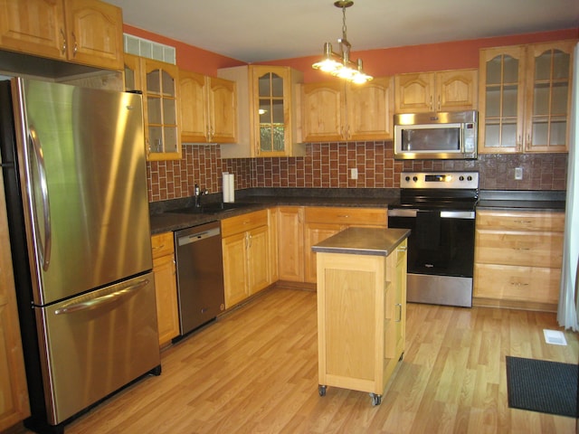 kitchen with hanging light fixtures, light wood-type flooring, tasteful backsplash, a kitchen island, and stainless steel appliances