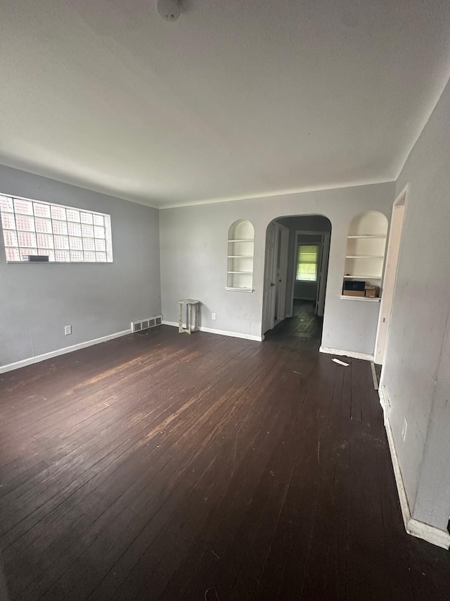 empty room with built in shelves and dark hardwood / wood-style flooring