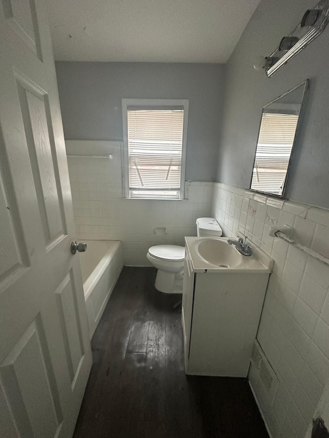 bathroom with a washtub, vanity, hardwood / wood-style flooring, tile walls, and toilet