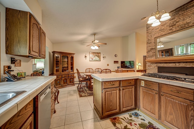 kitchen featuring tile countertops, ceiling fan with notable chandelier, vaulted ceiling, stainless steel dishwasher, and light tile patterned floors