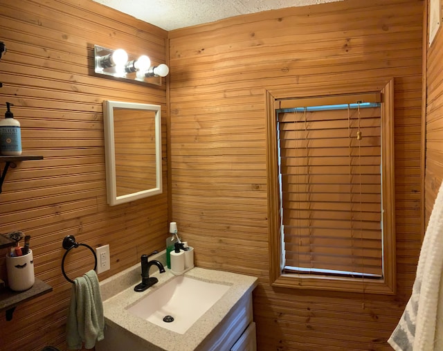 bathroom with a textured ceiling, vanity, and wooden walls