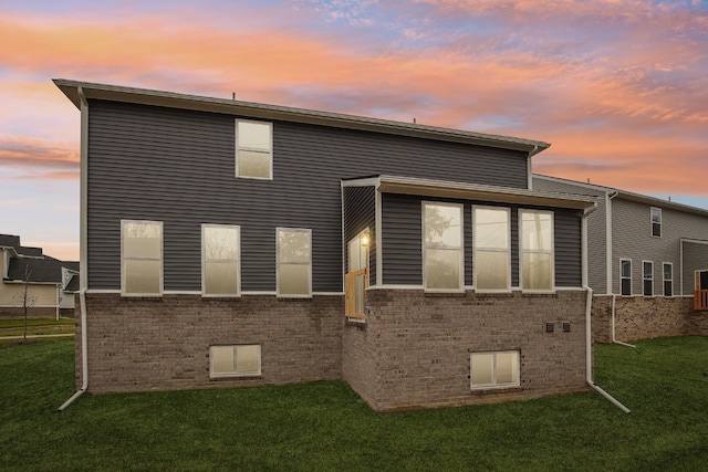 back house at dusk featuring a lawn