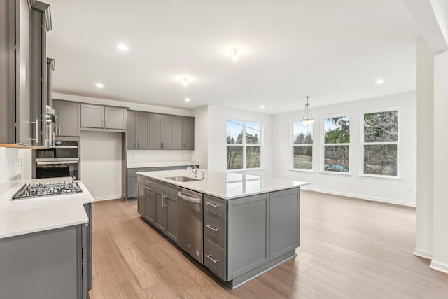 kitchen with a center island with sink, gray cabinets, stainless steel appliances, decorative light fixtures, and light wood-type flooring