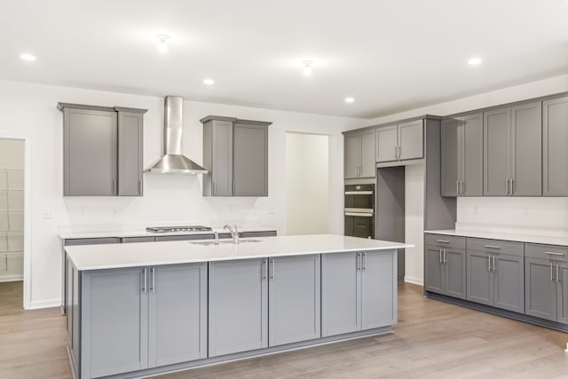 kitchen featuring sink, gray cabinetry, a center island with sink, and wall chimney range hood