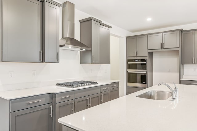 kitchen featuring gray cabinetry, appliances with stainless steel finishes, sink, and wall chimney range hood