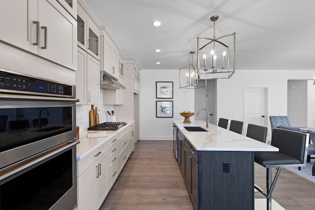 kitchen featuring a kitchen bar, stainless steel appliances, decorative light fixtures, a center island with sink, and white cabinets