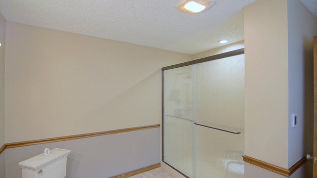 bathroom with a shower with shower door, a textured ceiling, and toilet