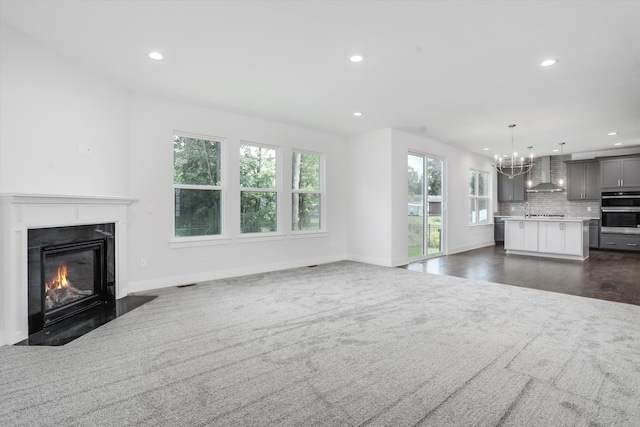 unfurnished living room featuring a high end fireplace, dark carpet, an inviting chandelier, and sink