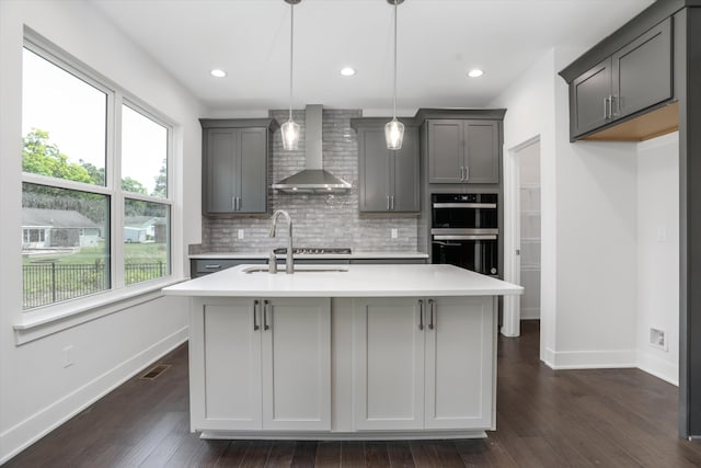 kitchen featuring wall chimney exhaust hood, dark hardwood / wood-style flooring, black double oven, decorative light fixtures, and gray cabinets