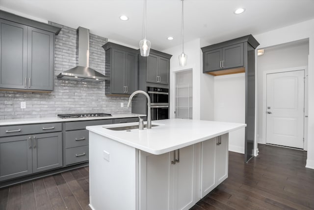 kitchen with pendant lighting, a kitchen island with sink, wall chimney exhaust hood, and gray cabinetry