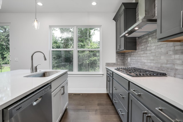 kitchen featuring pendant lighting, dark wood-type flooring, sink, wall chimney exhaust hood, and appliances with stainless steel finishes