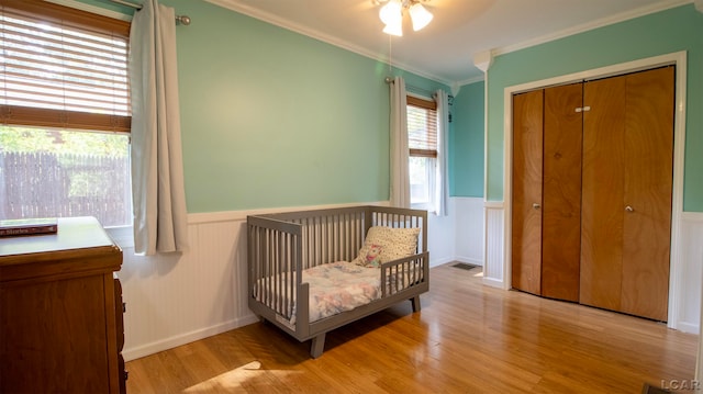 bedroom featuring a nursery area, light hardwood / wood-style floors, a closet, and crown molding