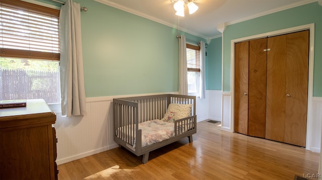 4241 Echo Cv, Manitou Beach, MI 49253 - bedroom featuring a wainscoted wall, light wood-style floors, crown molding, a crib, and a closet